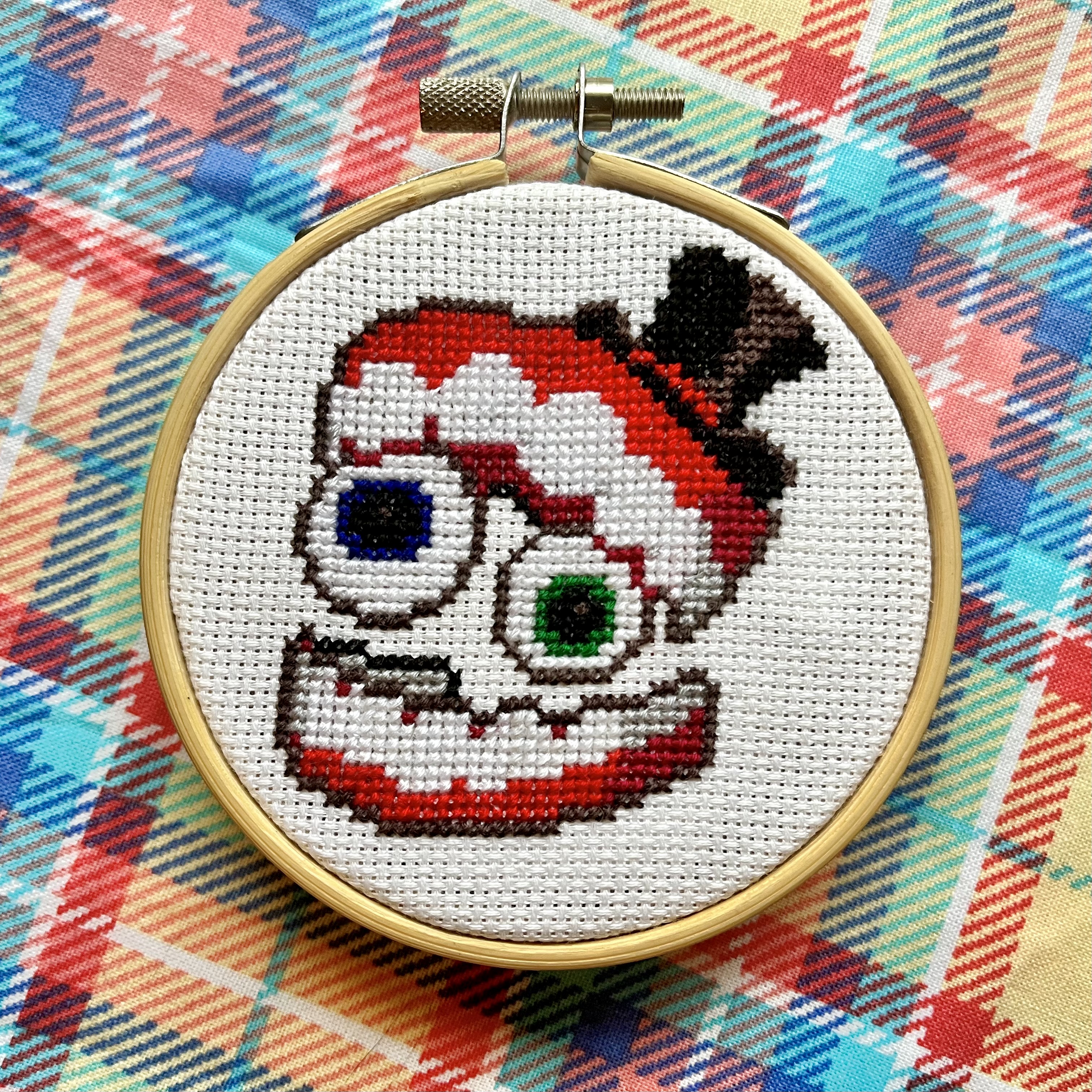 Cross-stitch of Caine from The Amazing Digital Circus in a wooden hoop, on white Aida cloth