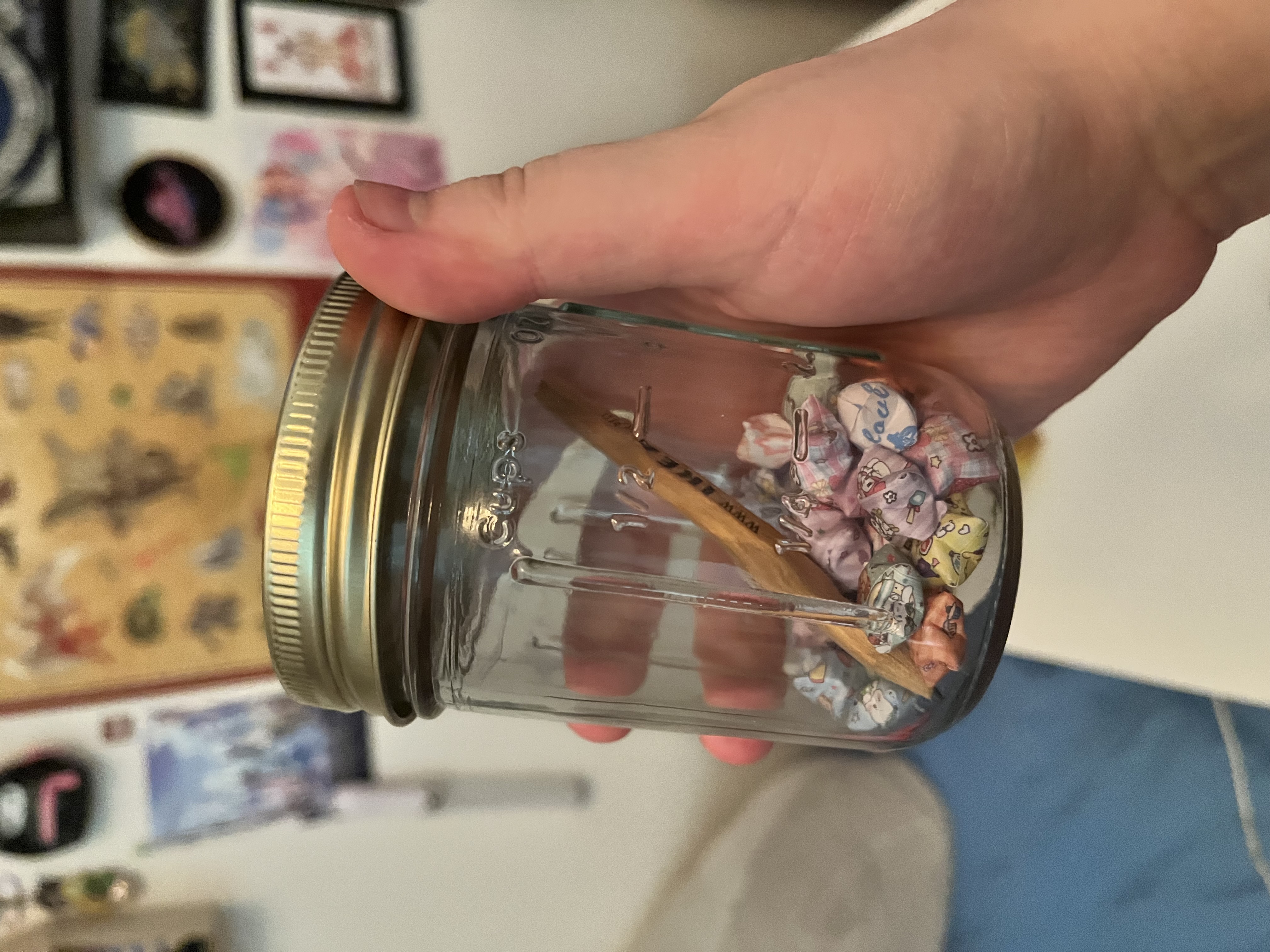 Glass mason jar held in hand, about one-quarter filled with small folded origami paper stars in colorful printed paper - the self-care star jar