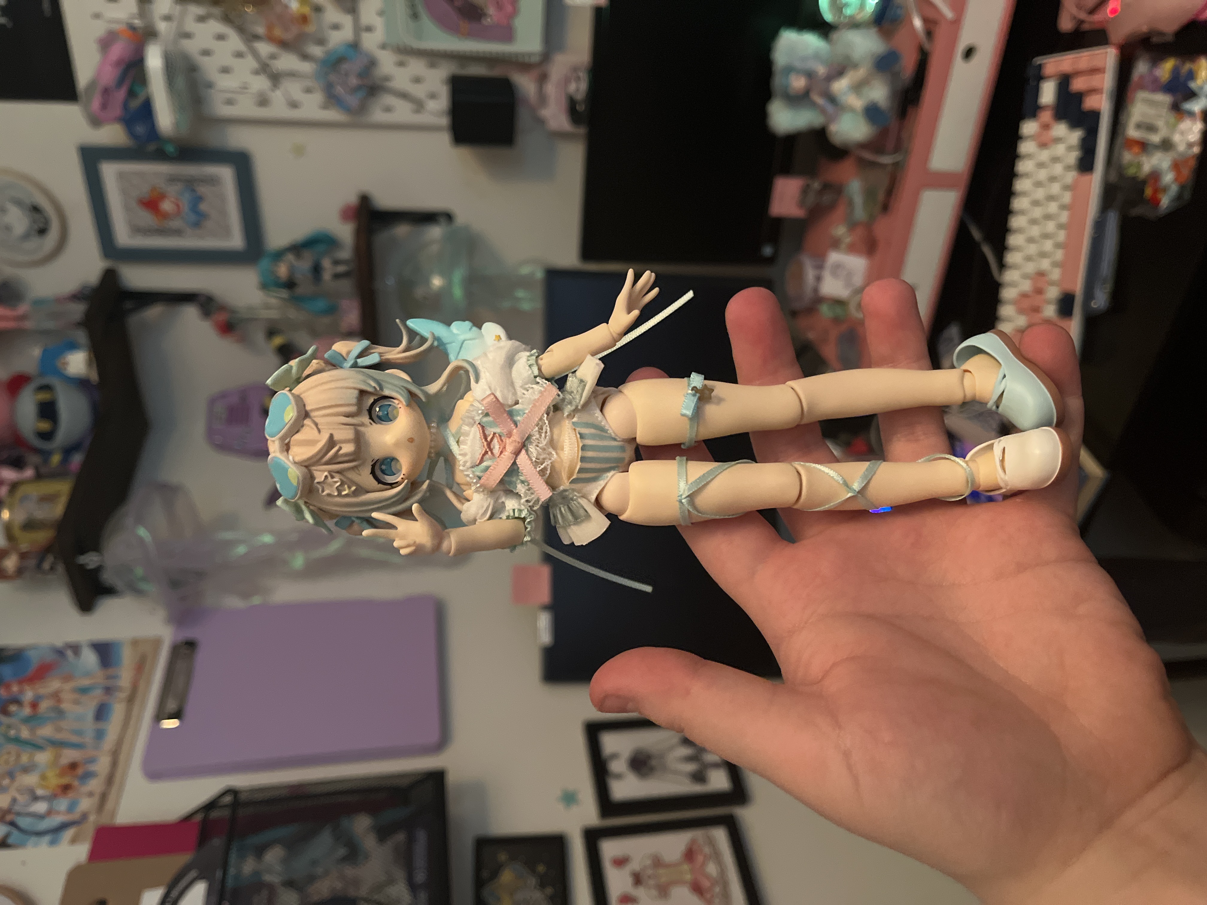Dreamy Lagoon secret rare Sugary Girls doll held in hand - small articulated figure with light blue twin bun hair, teal bows with star-print ribbons, pastel blue swimsuit, and detachable teal wings