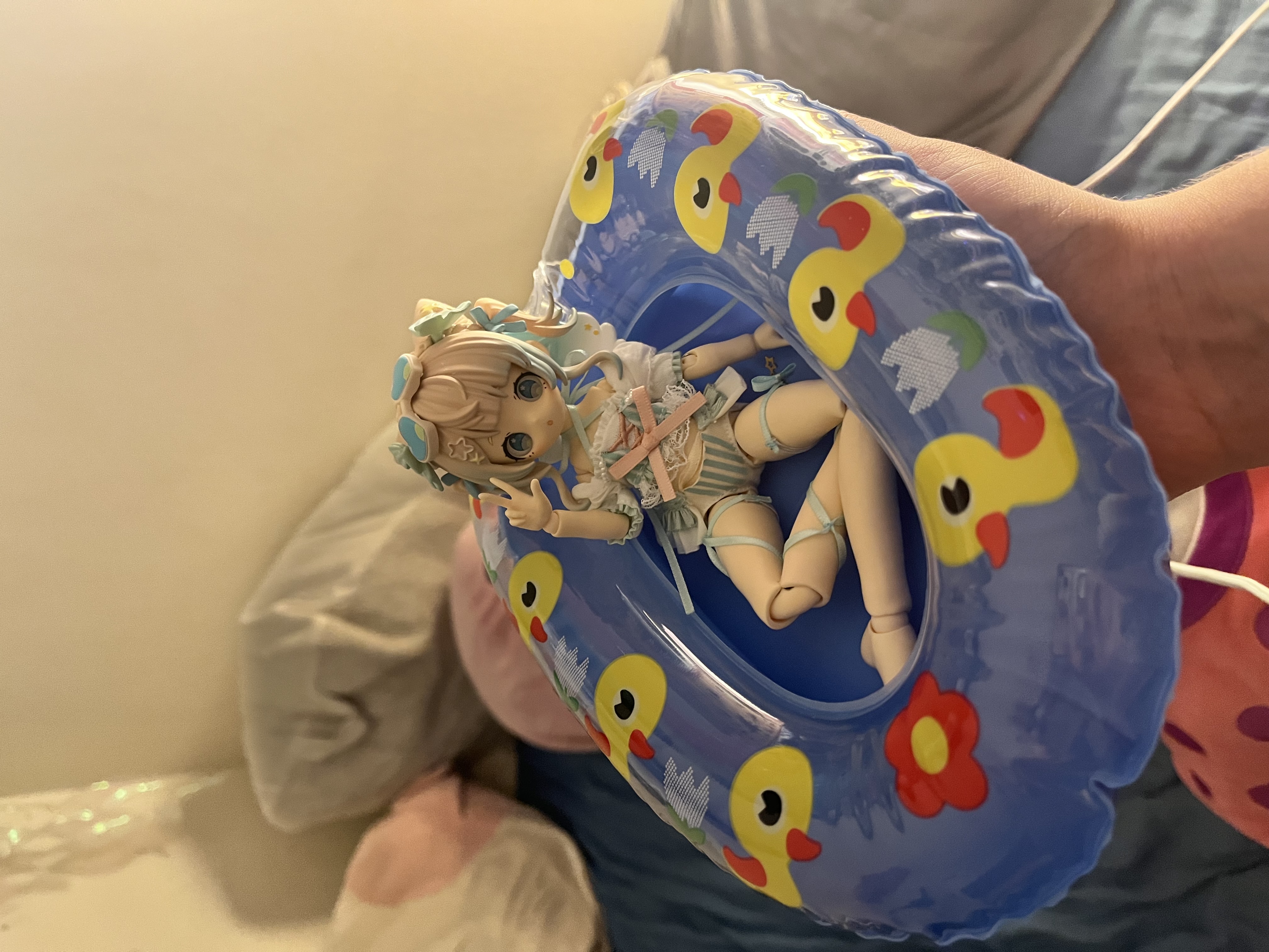 Dreamy Lagoon doll sitting inside a small inflatable pool float printed with yellow rubber ducks and flowers, held up to camera