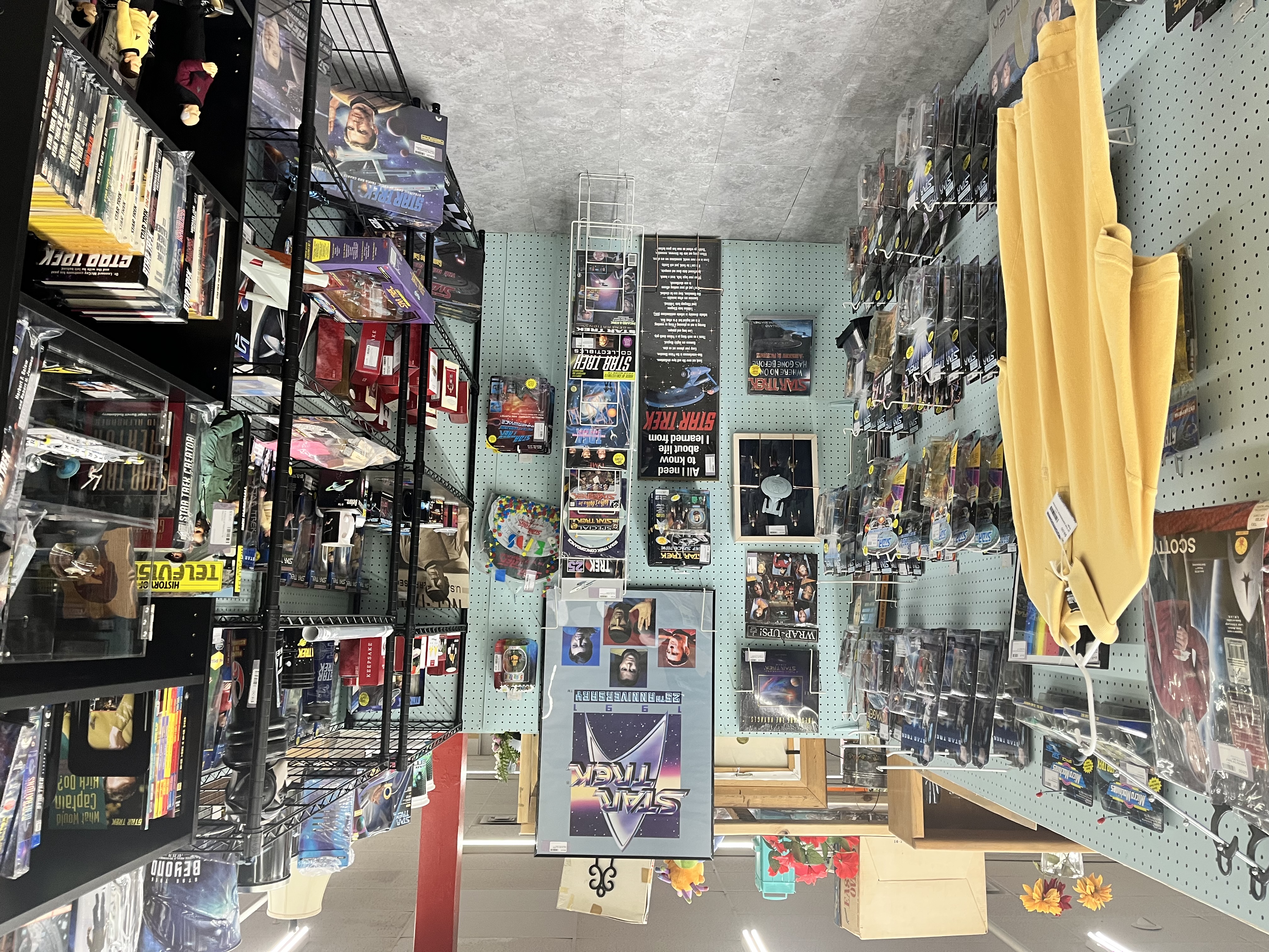 An antique mall booth packed floor-to-ceiling with Star Trek merchandise: VHS tapes, action figure boxes, framed posters, and collectibles on metal shelving racks